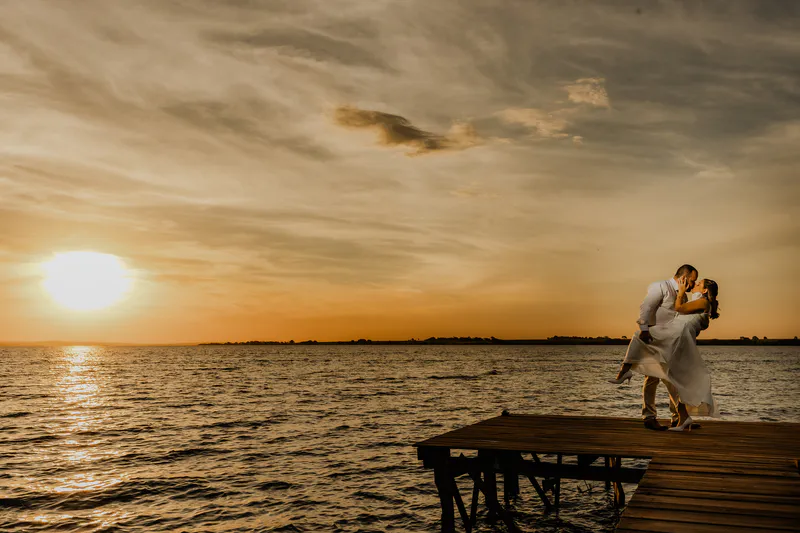 Casal se beijando num deck à beira d'água no pôr do sol